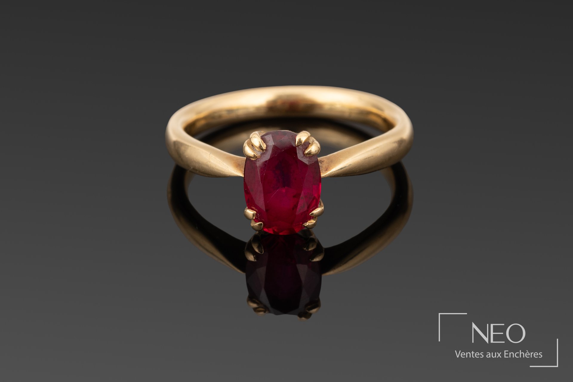 Bague en or jaune sertie d'une pierre rouge ovale sur fond gris