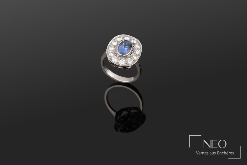 Bague en or blanc sertie d’un saphir ovale entouré de diamants sur fond noir