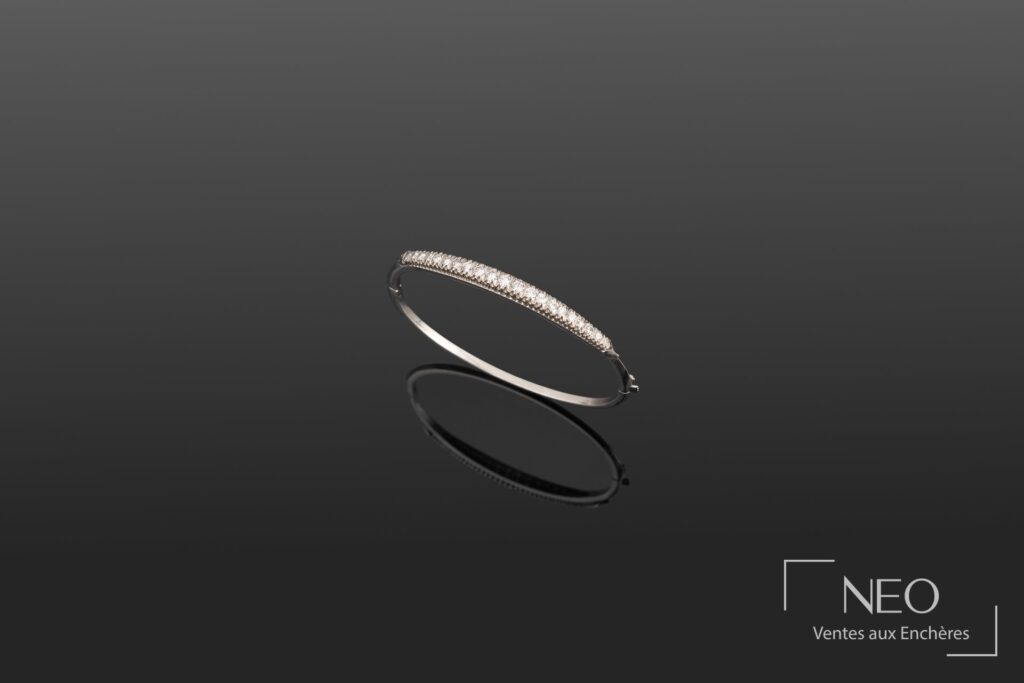 Bracelet rigide ouvrant en or blanc serti d’une ligne de diamants sur fond sombre