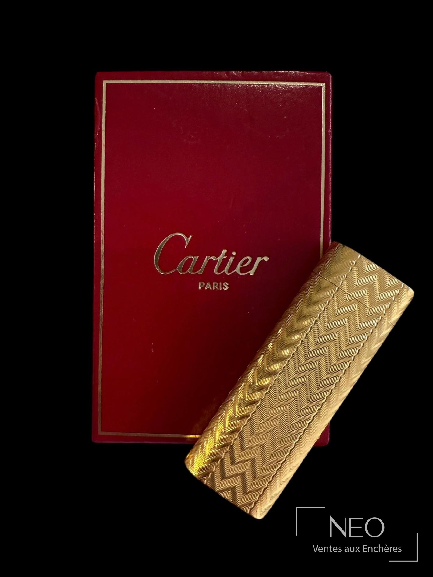 Briquet Cartier en métal doré devant son écrin rouge marqué Cartier Paris