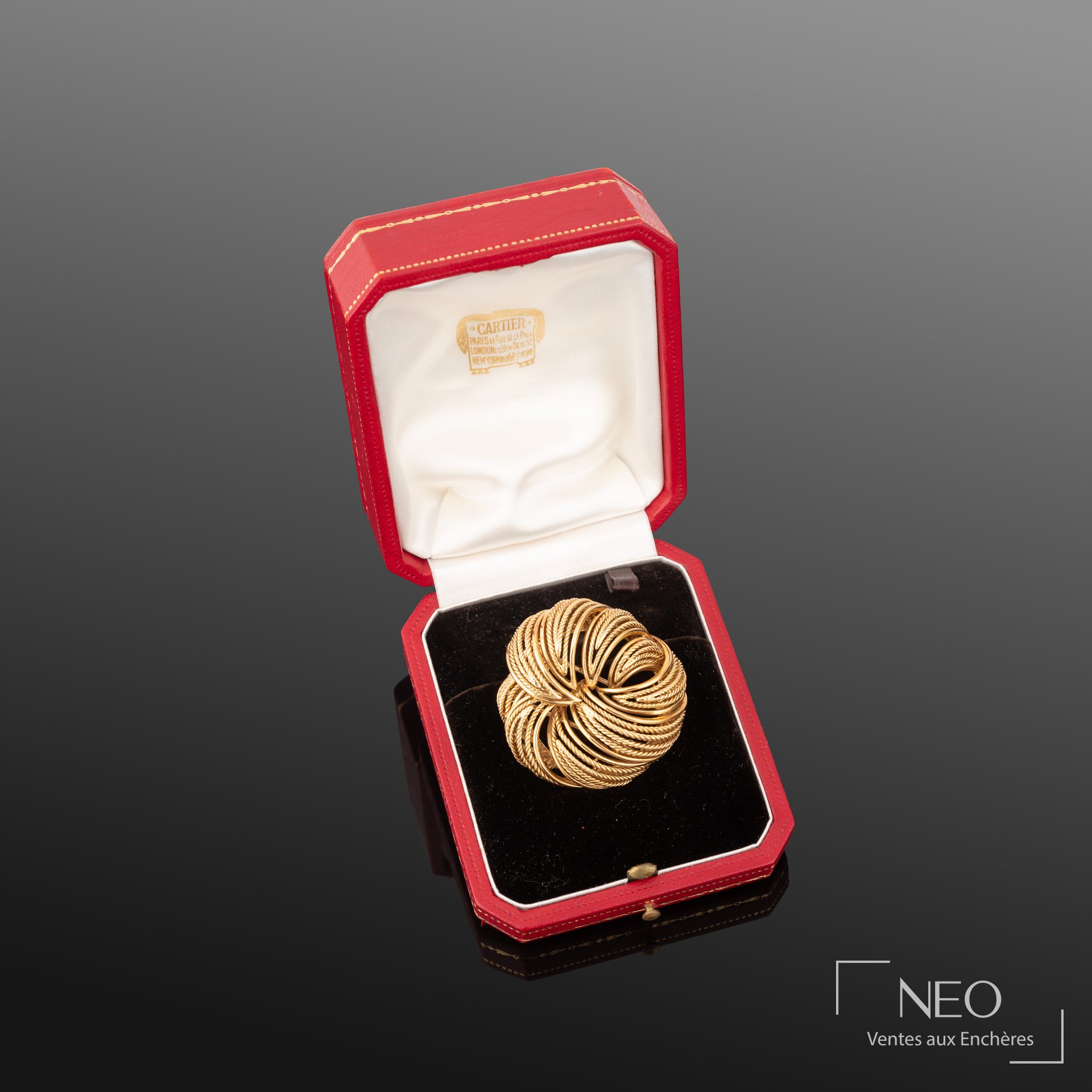 Broche Cartier ronde en or jaune présentée dans son écrin rouge et noir