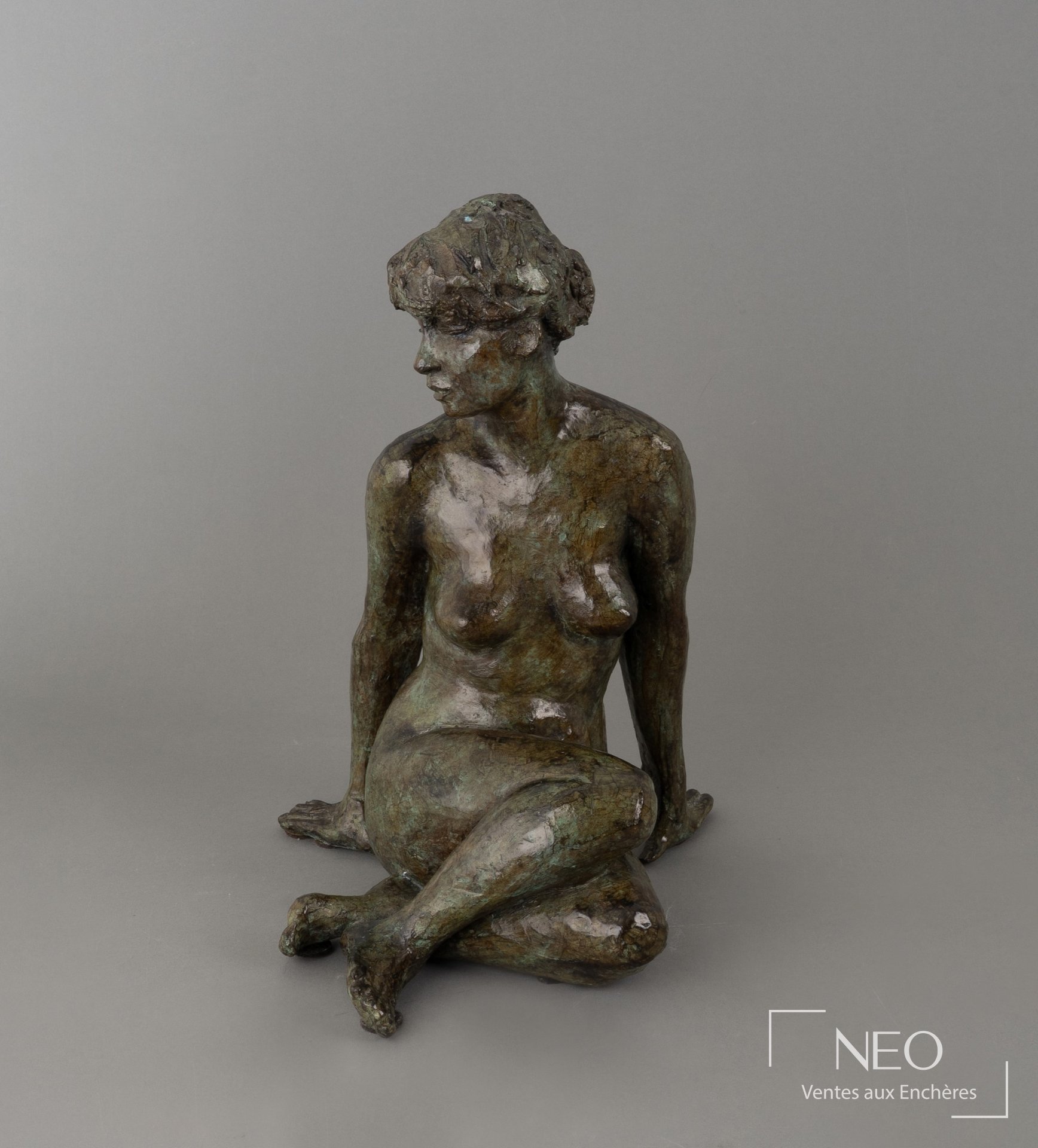 Sculpture en bronze à patine verte représentant une figure féminine assise de face.