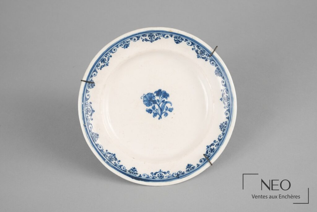 Assiette circulaire en faïence blanche à décor bleu de bouquet central et frise de rinceaux