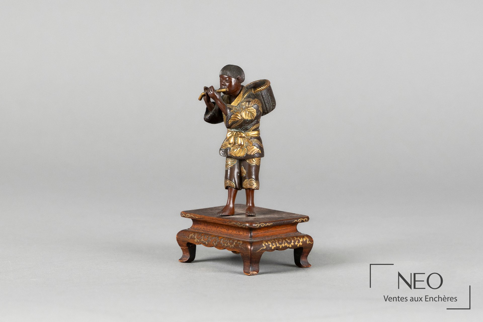 Okimono japonais en bronze représentant un joueur de flûte sur socle en bois décoré.